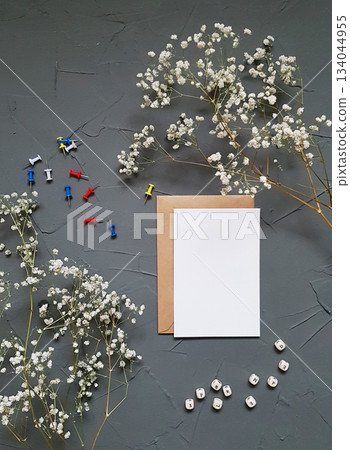 Minimalist flat lay with blank greeting card, dried baby s breath flowers, and colorful pins on gray textured background. Minimalist flat lay with blank greeting card, dried baby s breath flowers, and colorful pins on gray textured background. 134044955