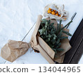 Top down winter scene of fir tree wrapped in kraft paper beside a mesh bag of oranges on snowy ground.  134044965