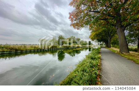 Tranquil fall scenery along quiet canal with rustling leaves and clouds Tranquil fall scenery along quiet canal with rustling leaves and clouds 134045084