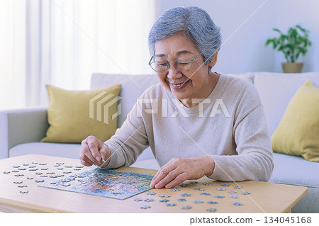 Senior woman doing a jigsaw puzzle in the living room Senior woman doing a jigsaw puzzle in the living room 134045168