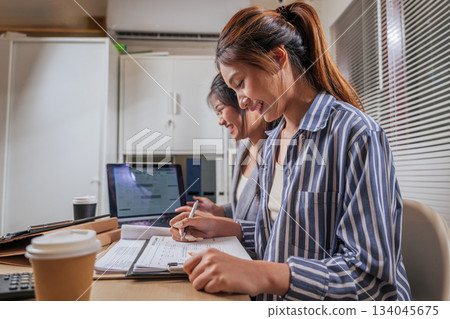 Young business women work online, learn at home office, team people collaborate on projects, focused woman writes monthly planner, smiling, productive office environment for busy working. 134045675