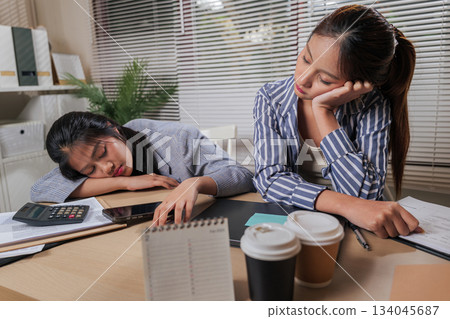 Young women business colleagues work from home office, team members showing exhaustion from online tasks, people feeling fatigue, needing rest after long hours, facing busy office day challenges. 134045687