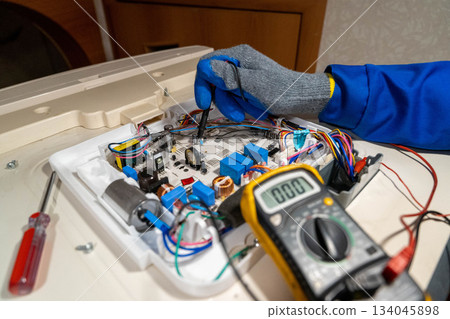 Worker repairs a circuit board with tools in a workshop during daytime hours 134045898