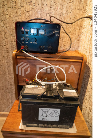 Battery charger and old battery located on wooden table in a room setting Battery charger and old battery located on wooden table in a room setting 134045925