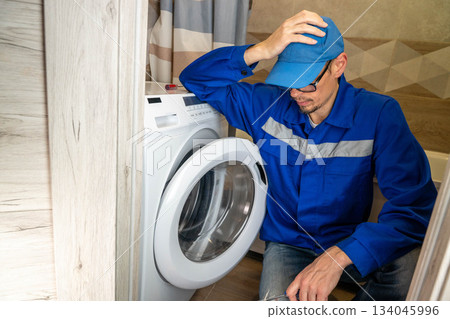 A home appliance repairman has difficulty repairing a home washing machine A home appliance repairman has difficulty repairing a home washing machine 134045996