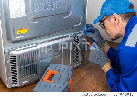 Repairing a refrigerator at home by a technician with blue gloves and tools Repairing a refrigerator at home by a technician with blue gloves and tools 134046012