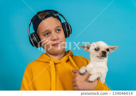 Young boy wearing headphones holds small dog against blue background 134046014