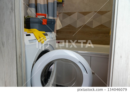 Washing machine in bathroom with tools and gloves ready for cleaning tasks Washing machine in bathroom with tools and gloves ready for cleaning tasks 134046079