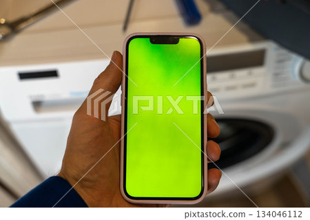A called home appliance repair technician uses a smartphone while repairing a home washing machine 134046112