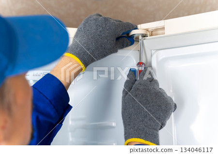 the serviceman adjusts the hinge of the door of the home refrigerator 134046117