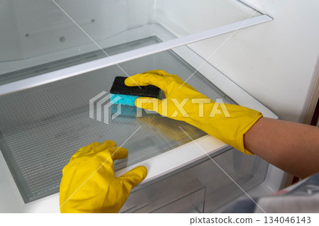 Person cleans the interior of a refrigerator with a sponge while wearing gloves Person cleans the interior of a refrigerator with a sponge while wearing gloves 134046143