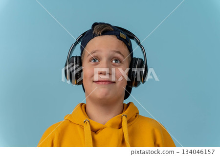 Young boy enjoys listening to music with headphones in a light blue setting 134046157
