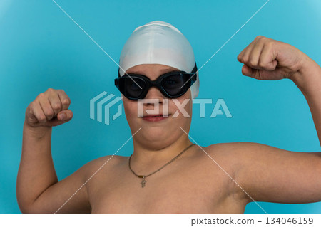 Young swimmer poses with confidence in swimming gear against a blue background 134046159