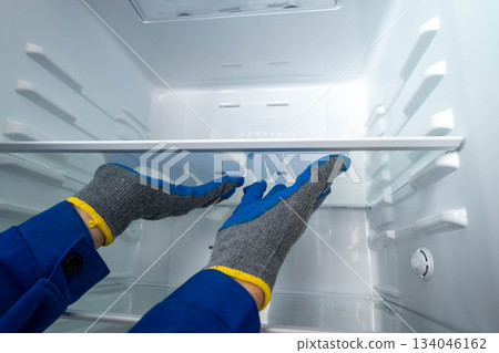Worker in blue gloves installs a shelf in an empty refrigerator at a repair shop 134046162
