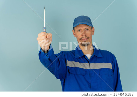 Man holds screwdriver in workshop environment during daytime with blue background 134046192