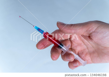 Hand holds a syringe filled with red liquid during a medical procedure in a clinic Hand holds a syringe filled with red liquid during a medical procedure in a clinic 134046198