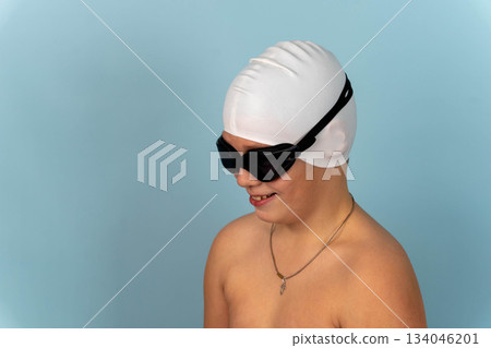 Young swimmer prepares for practice with swim cap and goggles in indoor pool area 134046201
