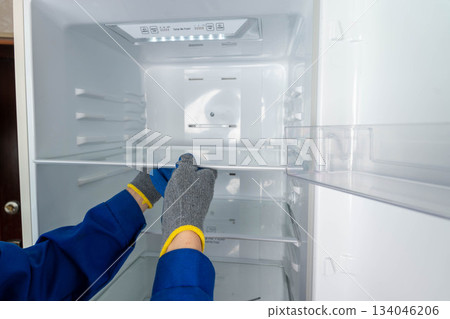 Repair technician organizes shelves inside a refrigerator in a kitchen setting Repair technician organizes shelves inside a refrigerator in a kitchen setting 134046206