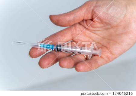 Hand holding a syringe with a blue tip in a neutral setting at a medical facility 134046216
