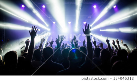 Crowd of people with hands raised at music concert or festival, enjoying live show with bright white and purple stage lights and smoke Crowd of people with hands raised at music concert or festival, enjoying live show with bright white and purple stage lights and smoke 134046318