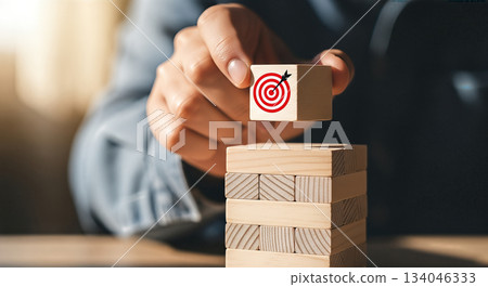 hand placing wooden block with red target symbol on top of stack strategy planning goal achievement business focus precision concept 134046333