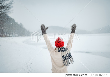 Rear view of woman enjoying snowfall in winter landscape. 134046363