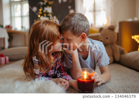 Siblings in pyjamas lying on floor, looking at candle. Christmas atmosphere. Siblings in pyjamas lying on floor, looking at candle. Christmas atmosphere. 134046379