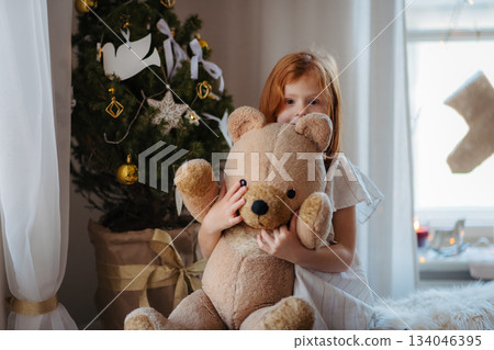 Small girl hugging teddy bear. Christmas mood at home. 134046395