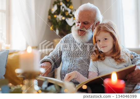 Small children with senior grandfather indoors at home at Christmas, looking at photographs. Small children with senior grandfather indoors at home at Christmas, looking at photographs. 134046399