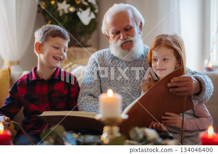 Small children with senior grandfather indoors at home at Christmas, looking at photographs. Small children with senior grandfather indoors at home at Christmas, looking at photographs. 134046400