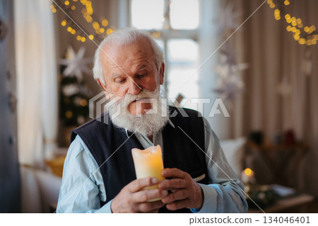 Front view of happy senior man with candle indoors at home at Christmas. Front view of happy senior man with candle indoors at home at Christmas. 134046401