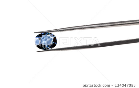 A blue gemstone is being held up by a jeweler's loupe 134047083