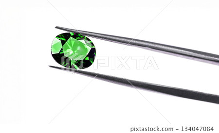 A green gemstone is being held up by a metal tool 134047084