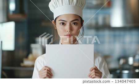 A Japanese female chef holding up a white piece of paper with a serious face A Japanese female chef holding up a white piece of paper with a serious face 134047405