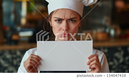Caucasian female chef angry and holding up a white piece of paper Caucasian female chef angry and holding up a white piece of paper 134047410