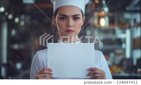 Caucasian female chef holding up a white piece of paper with a serious face Caucasian female chef holding up a white piece of paper with a serious face 134047411