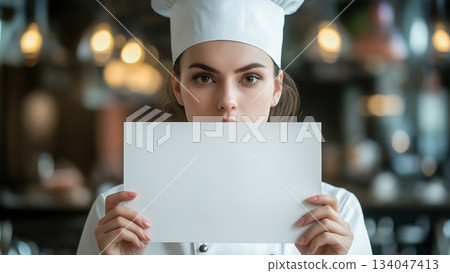Caucasian female chef looking straight ahead and holding up a white piece of paper Caucasian female chef looking straight ahead and holding up a white piece of paper 134047413
