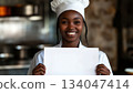 Smiling black female chef holding up a white piece of paper 134047414