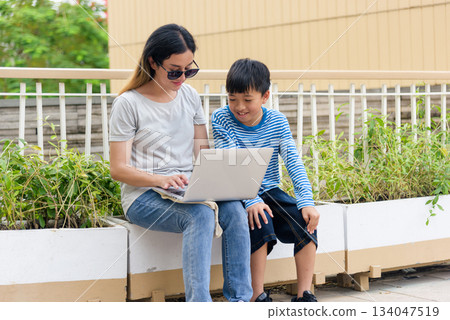 Mother child summer city family woman people parent son enjoy warm bonding time outdoors, engaging with laptop for interaction on urban street, parent guiding smiling son in relaxed summer activity. Mother child summer city family woman people parent son enjoy warm bonding time outdoors, engaging with laptop for interaction on urban street, parent guiding smiling son in relaxed summer activity. 134047519