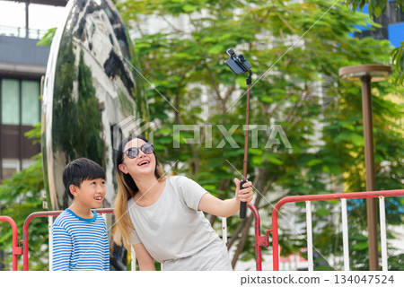 Happy mother son family enjoys summer city street activity, parent woman child people capture joyful moment with smartphone selfie stick, urban city lifestyle. Happy mother son family enjoys summer city street activity, parent woman child people capture joyful moment with smartphone selfie stick, urban city lifestyle. 134047524