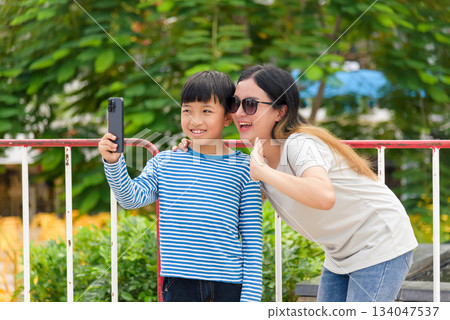 Mother child summer city family woman people street parent son enjoy outdoor fun, joyful woman with young boy capture happy moment using mobile phone, sunny urban green space. 134047537