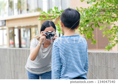 Mother and son, family people, enjoy summer city street activity, woman photographs child with vintage camera, capturing urban outdoor moments, creating happy memories during warm weather fun. 134047540