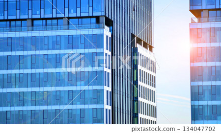 Structural glass wall reflecting blue sky. Abstract modern architecture fragment. Glass building with transparent facade of the building and blue sky. Contemporary architectural background. 134047702