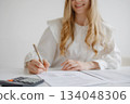 Person reviewing documents with a calculator on a desk during a work session in a bright office setting 134048306