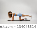 Woman performing a core-strengthening exercise on a yoga mat in a bright studio during daytime 134048314