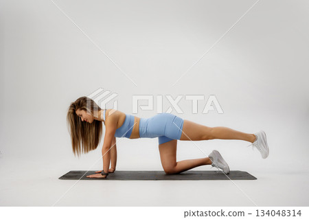 Woman performing a core-strengthening exercise on a yoga mat in a bright studio during daytime 134048314