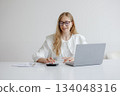 Young woman working on laptop with calculator during daytime in a minimalistic workspace 134048316