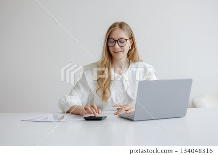 Young woman working on laptop with calculator during daytime in a minimalistic workspace Young woman working on laptop with calculator during daytime in a minimalistic workspace 134048316