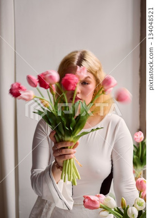 Elegant blonde woman gazing amidst tulip arrangement in studio 134048521