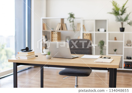 A laptop sits on a wooden desk in a bright, modern office setting, ready for work A laptop sits on a wooden desk in a bright, modern office setting, ready for work 134048655